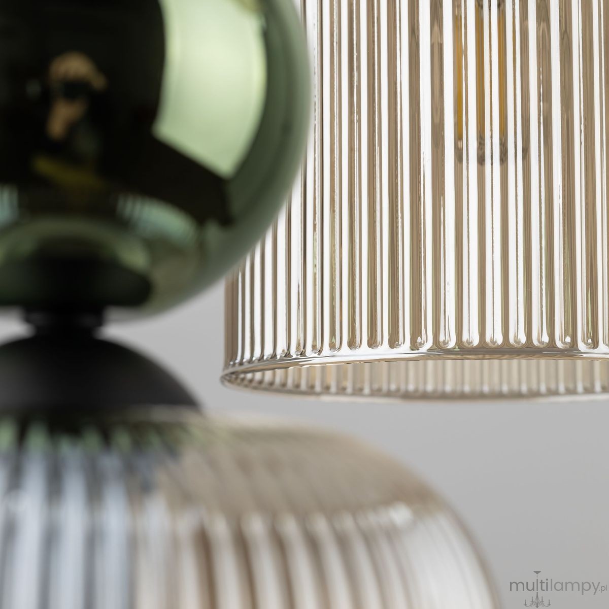 Lampa wisząca Sophia 6xE14 w kolorze bursztynowym i zielonym, z przezroczystymi, żebrowanymi kloszami. Ujęcie z bliska na detale kloszy i górną część lampy, z czarną podstawą oraz błyszczącą, zieloną dekoracją.
