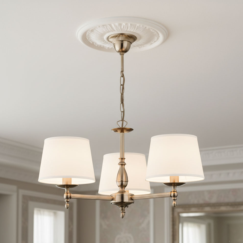 Żyrandol Roksana 3-punktowy w kolorze złotym z trzema białymi kloszami. Ujęcie z dołu, wiszący na łańcuchu, z ozdobnym stropem. Klosze mają cylindryczny kształt, materiał tekstylny, a konstrukcja metalowa. Idealny do eleganckich wnętrz.