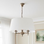 Żyrandol Roksana 3-punktowy w kolorze białym z metalowymi detalami. Okrągły klosz podwieszony na łańcuszku, z trzema źródłami światła. Widok frontalny, z tłem w jasnych odcieniach. Idealny do eleganckich wnętrz.