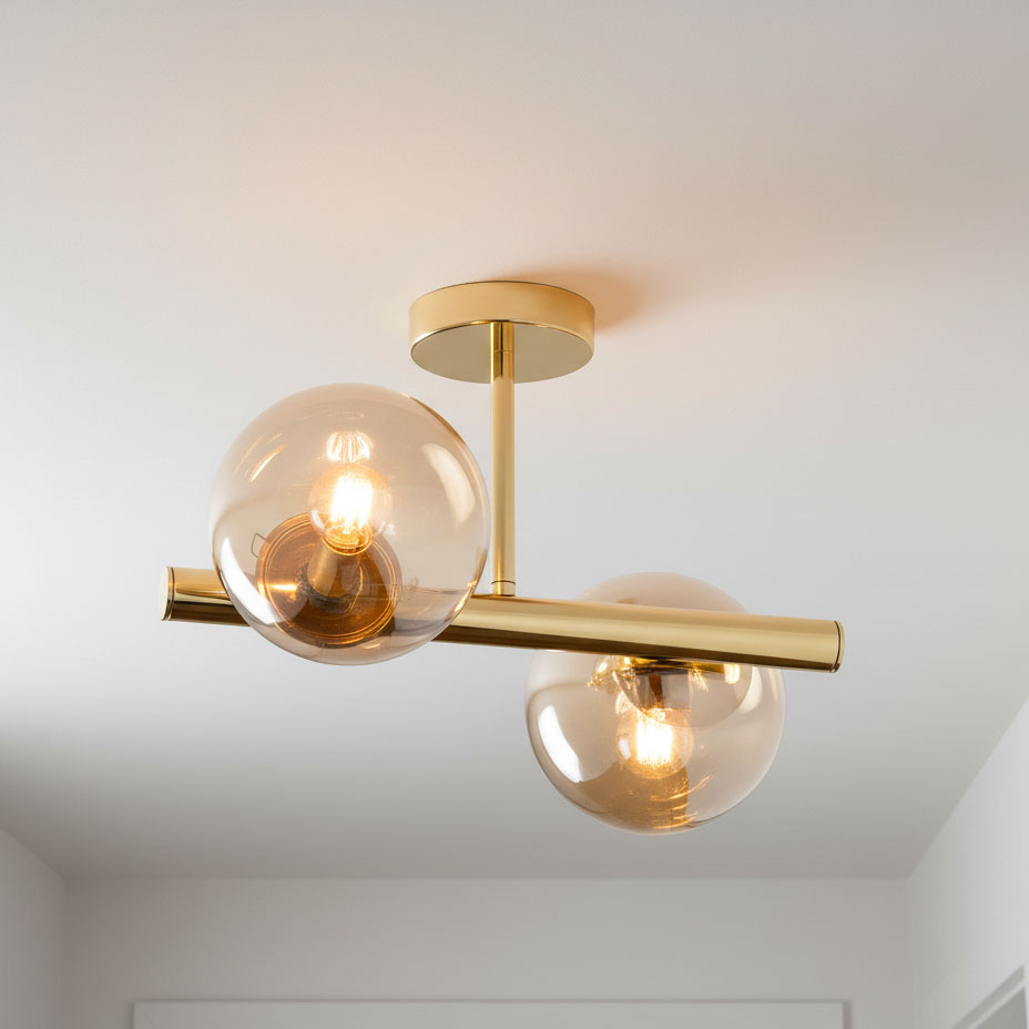 Lampa sufitowa Eral 2-punktowa w kolorze złotym, z przezroczystymi kulistymi kloszami. Ujęcie z dołu, ukazujące dwa źródła światła zamocowane na poziomej rurze. Elementy metalowe mają błyszczące wykończenie. Tło jasne, jednolite.