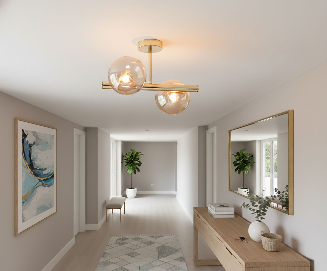 Złota lampa sufitowa Eral 2-punktowa z przezroczystymi kloszami, umieszczona centralnie w jasnym pomieszczeniu. Lampa ma prostą, nowoczesną konstrukcję i oświetla przestrzeń. W tle widoczna roślinność oraz dekoracje na ścianach.