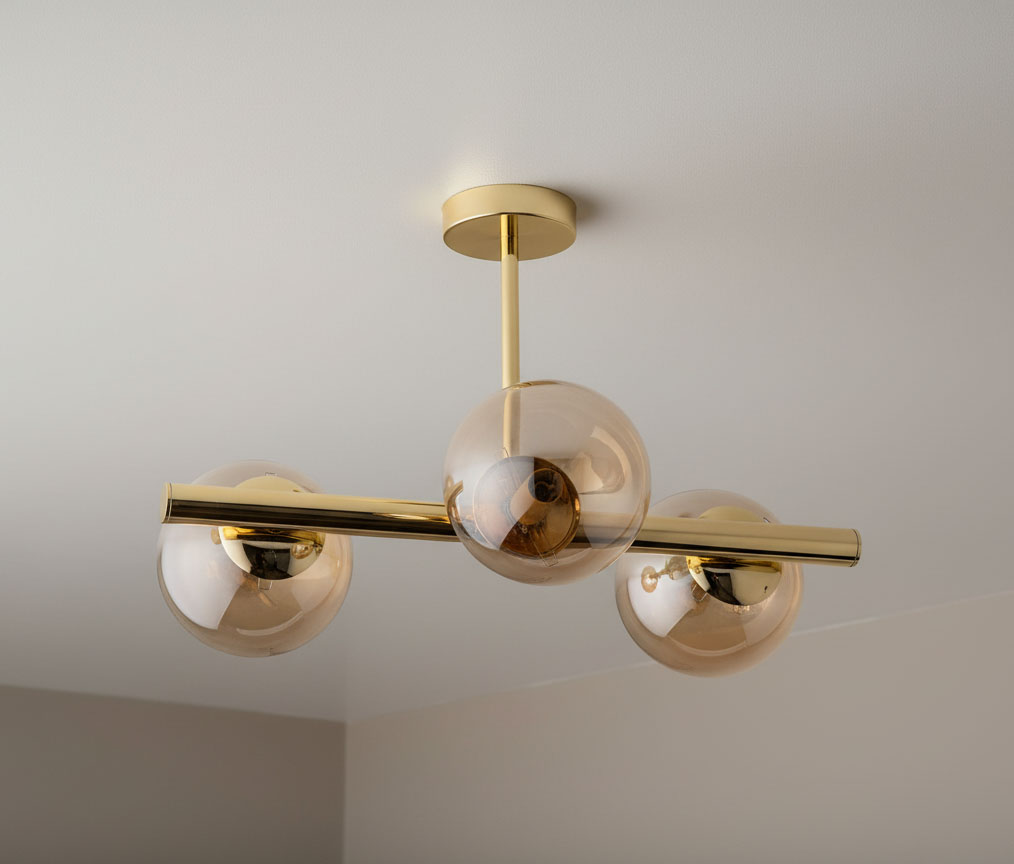 Złota lampa sufitowa Eral z trzema kulistymi kloszami. Ujęcie z dołu, pokazujące metalową konstrukcję i przezroczyste, lekko brązowe kulki. Lampa zamontowana do sufitu, w nowoczesnym stylu.