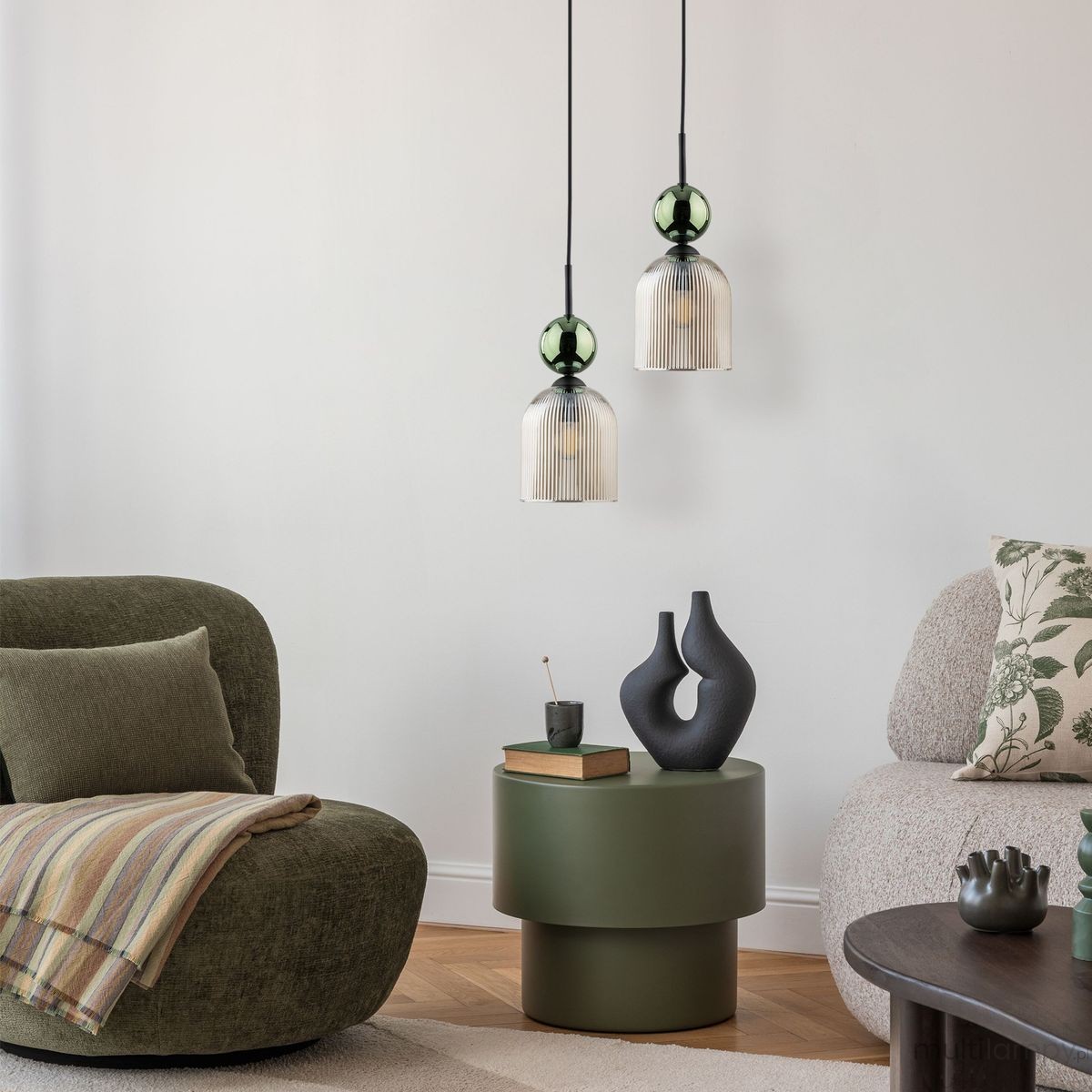 Lampa wisząca Sophia 1xE14, z bursztynowym kloszem i zieloną kulą, zawieszona na czarnym przewodzie. W tle widoczny nowoczesny salon z zielonym fotelem, okrągłym stołem i dekoracjami w neutralnych kolorach.