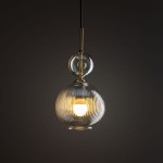 Lampa wisząca Sophia z jednym źródłem światła E14, z bursztynowym, żłobkowanym kloszem w kształcie kulistym oraz przezroczystą górną częścią. Zawieszona na cienkim, czarnym przewodzie, z metalowymi elementami w kolorze złotym.