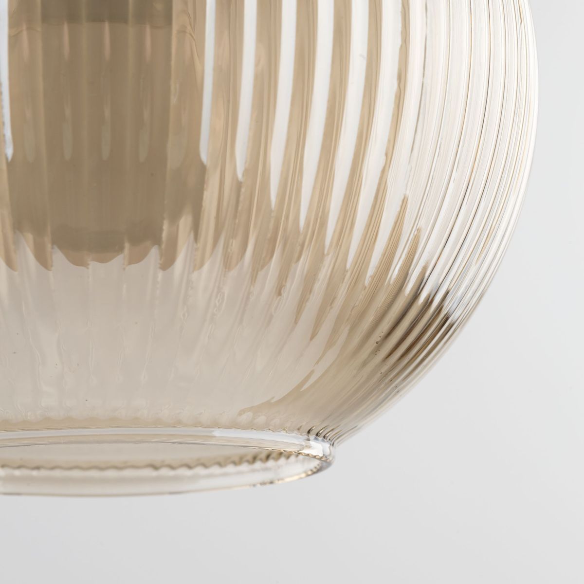 Lampa wisząca Sophia z bursztynowego, teksturowanego szkła, z widocznymi delikatnymi żłobieniami. Ujęcie z dołu, zbliżenie na klosz, który jest okrągły i lekko przezroczysty, zawieszony na cienkim przewodzie.