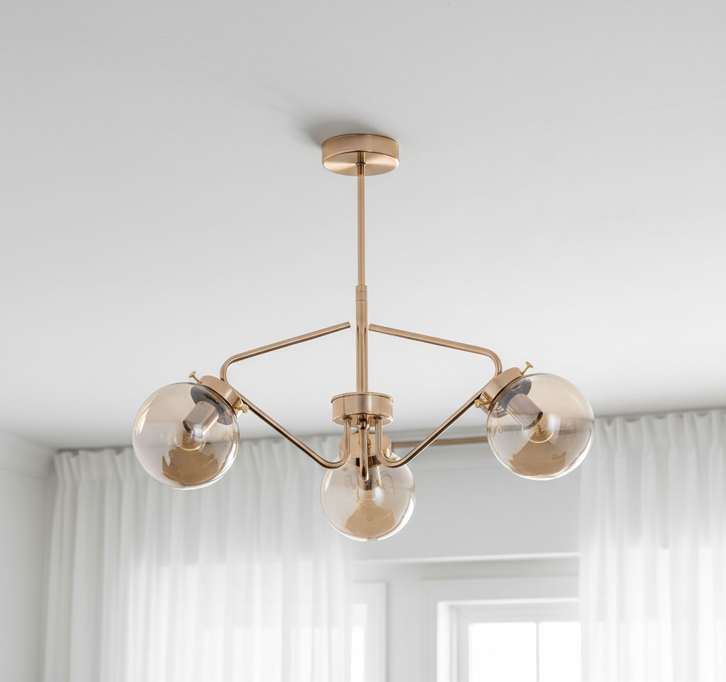 Lampa wisząca Barsum w kolorze złotym, 3-punktowa, z przezroczystymi kulistymi kloszami. Ujęcie z dołu, pokazujące całą konstrukcję oraz detale mocowania do sufitu. Prosta aranżacja w tle z białymi zasłonami.