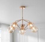 Lampa wisząca Barsum 5-punktowa w kolorze złotym. Posiada pięć szklanych kloszy w formie kul, zamontowanych na metalowej konstrukcji. Ujęcie z góry, w jasnym wnętrzu z białymi zasłonami.