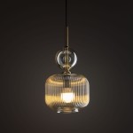 Lampa wisząca Sophia z kloszem w bursztynowym kolorze, z przezroczystym szklanym elementem u góry. Posiada jedno gniazdo E14. Zawieszona na czarnym przewodzie, w stylu nowoczesnym, z wyraźnym żłobieniem na kloszu. Tło ciemne.