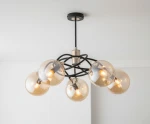 Lampa wisząca Doxa 5-punktowa w kolorze czarnym z elementami złotymi. Okrągłe, przezroczyste klosze w kształcie kul, umieszczone na czarnym, metalowym stelażu, zwisającym z sufitu. Nowoczesny design, idealna do różnych wnętrz.