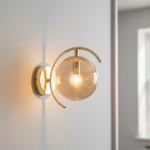 Kinkiet El Dorado 1-punktowy w kolorze złotym, z okrągłą, przezroczystą kloszem wykonanym z szkła. Produkt zamontowany na ścianie, z dekoracyjnym, zaokrąglonym uchwytem. Widoczna żarówka w środku klosza, emitująca ciepłe światło.