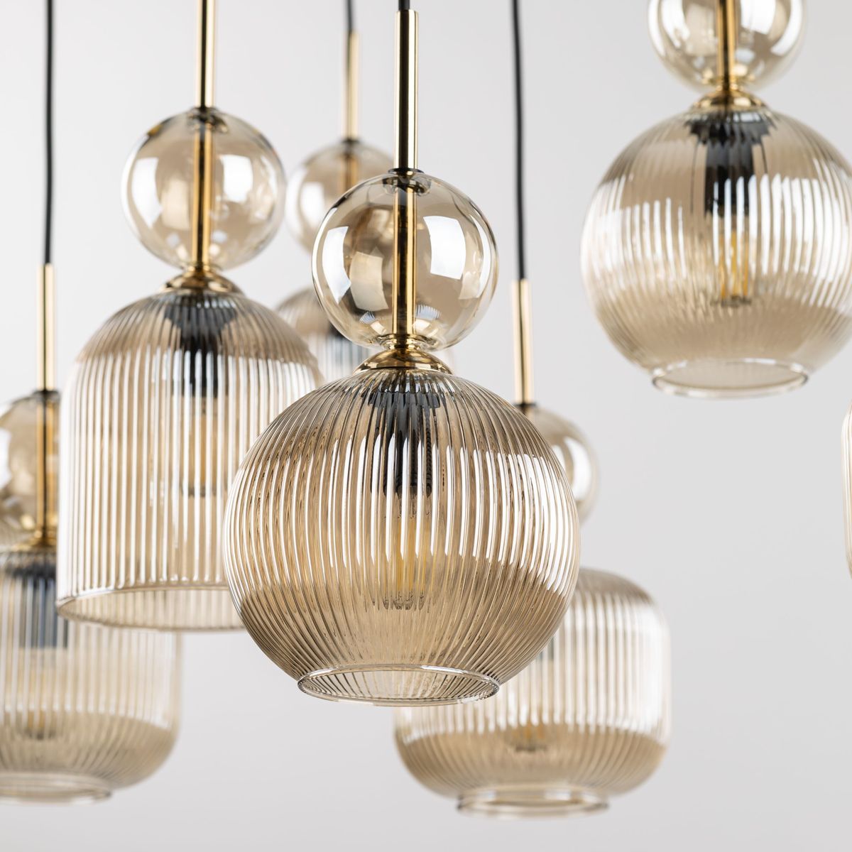 Lampa wisząca Sophia z pięcioma kloszami E14 w bursztynowym kolorze, z przezroczystego, teksturowanego szkła. Klosze mają różne kształty: kulisty i cylindryczny, z metalowymi elementami w złotym odcieniu, zawieszone na czarnych przewodach.
