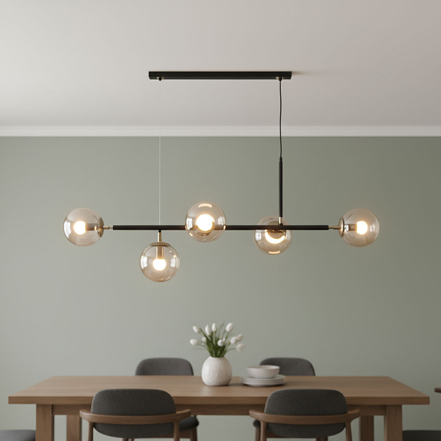Lampa wisząca Dansa 5-punktowa w kolorze czarnym i złotym, z pięcioma przezroczystymi kloszami, zawieszona na długim, prostokątnym stelażu. Zainstalowana nad drewnianym stołem w jadalni, na jednolitym, zielonym tle.
