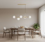 Lampa wisząca Dansa w kolorze złota i białego, z pięcioma okrągłymi kloszami, zawieszona nad drewnianym stołem w jasnym wnętrzu. W tle widoczne krzesła z jasnym obiciem i roślina doniczkowa.