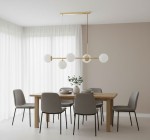 Lampa wisząca Dansa z pięcioma punktami świetlnymi, w złotym kolorze z białymi kloszami. Zawieszona nad drewnianym stołem w jasnym wnętrzu, z szarymi krzesłami i roślinnością w tle. Kąt ujęcia frontalny, pokazujący detale i proporcje.