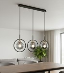 Lampa wisząca Akira 3-punktowa w kolorze czarnym i złotym. Składa się z trzech szklanych kloszy w metalowych obręczach, zawieszonych na czarnych linkach. Produkt umieszczony nad stołem w jasnym wnętrzu z rośliną w tle.