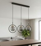 Lampa wisząca Akira 3-punktowa w kolorze czarnym i złotym. Posiada trzy szklane klosze w okrągłych ramkach, zawieszone na czarnych kablach. Ujęcie z góry, z widokiem na stół i kanapę w tle, tworząc elegancką aranżację wnętrza.