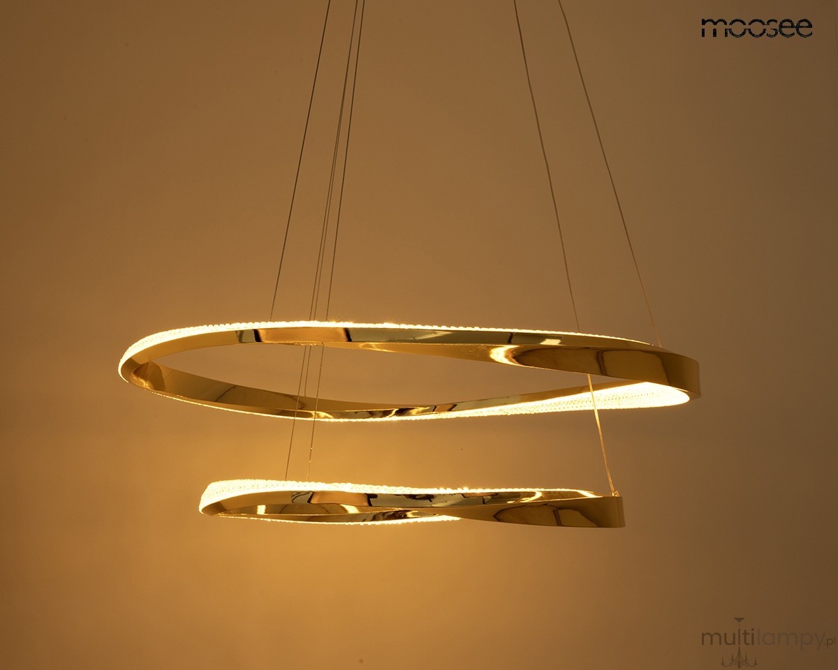 Lampa wisząca Anillo 2xLED 41W w kolorze złotym, składająca się z dwóch okrągłych pierścieni. Ujęcie z boku, zawieszona na cienkich linkach. Emituje ciepłe światło (3000K) i ma gładką, błyszczącą powierzchnię. Tło jasne, jednolite.