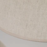 Beżowa lampa wisząca Coena Sabia z trzema miejscami na żarówki E27. Klosz wykonany z tkaniny o delikatnej, teksturowanej powierzchni, wykończony subtelną tasiemką. Ujęcie z bliska, skupiające się na detalu tkaniny.