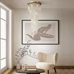 Lampa sufitowa Cascade 12-punktowa DIA522-CL-12-G z wiszącymi kryształkami, złotym stelażem, w aranżacji wnętrza. Produkt zawieszony w centralnej części pomieszczenia, w otoczeniu jasnych ścian oraz minimalistycznych mebli.