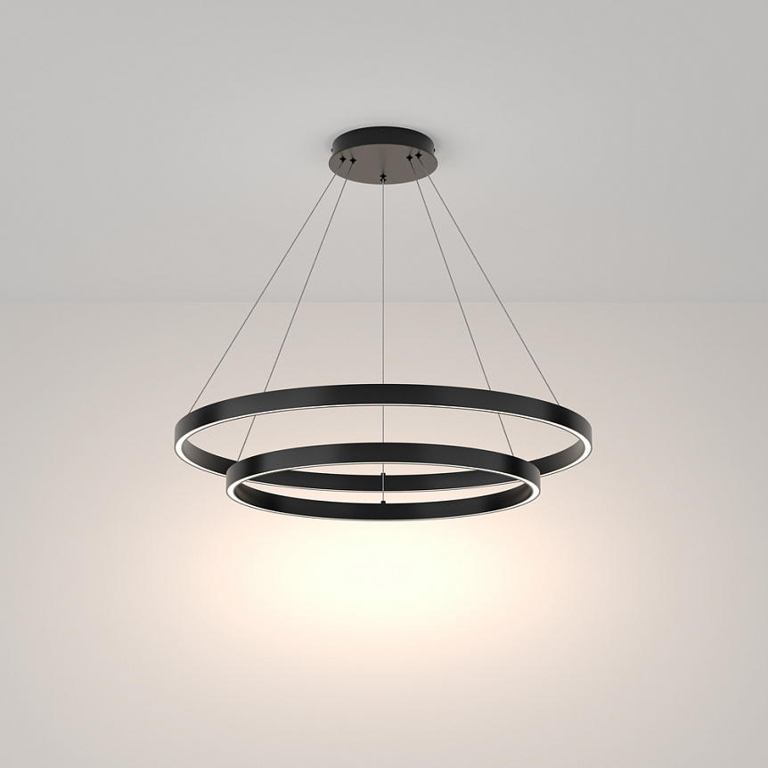 Czarna lampa wisząca Rim 4000K z dwoma okrągłymi pierścieniami, zawieszona na cienkich linkach. Górny pierścień jest większy, dolny mniejszy. Emituje jasne światło, idealna do nowoczesnych wnętrz. Tło jasne, jednolite.