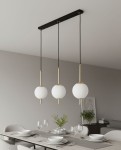 Lampa wisząca Diora 3xE14 w kolorze czarno-złotym, z trzema białymi kulistymi kloszami zawieszonymi na cienkich, czarnych linkach. Produkt zamontowany na prostokątnej, czarnej podstawie. Widoczne tło z drewnianym stołem i zastawą stołową.