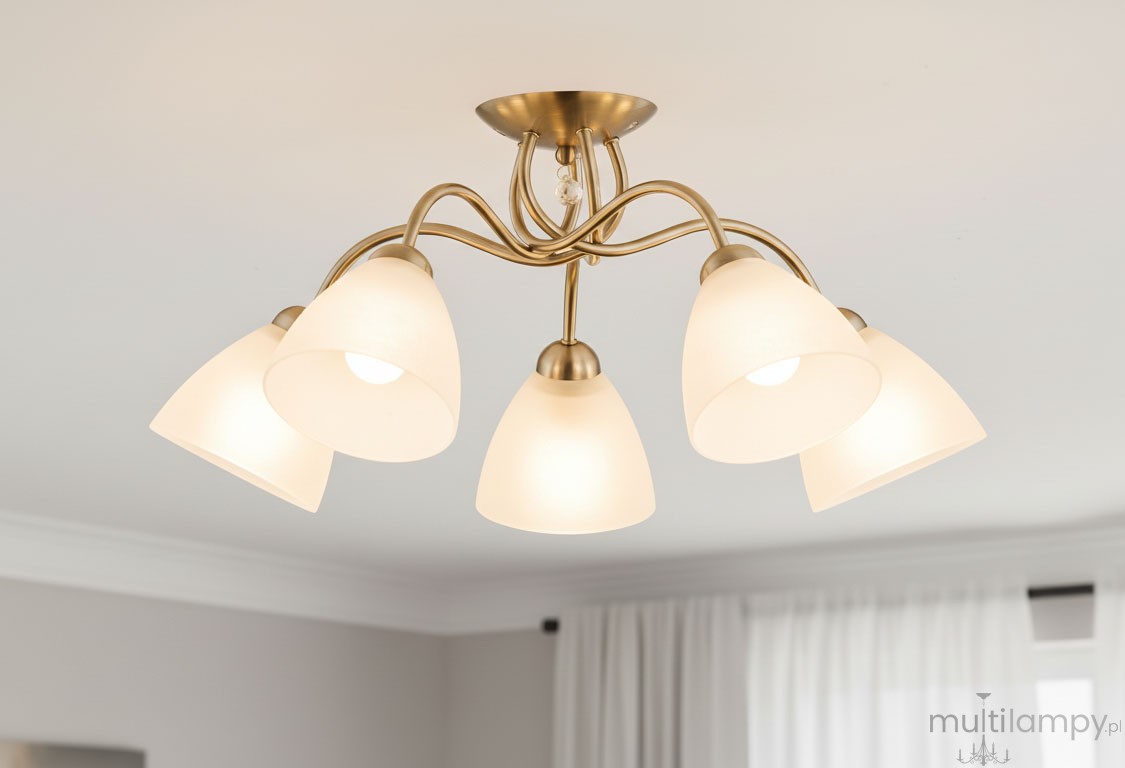 Lampa sufitowa Amarillo Patyna 5-punktowa w kolorze złotym z pięcioma alabastrowymi kloszami w kształcie stożka. Ujęcie z dołu, montowana na suficie, z eleganckimi, falującymi ramionami. Tło jasne, z zasłonami w oknie.