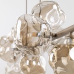 Lampa wisząca Lava Sabia w kolorze beżowym, z dziewięcioma kloszami w kształcie kul z przezroczystego szkła. Widoczne źródła światła G9 oraz metalowa konstrukcja. Klosze nawiązują do organicznych form. Tło białe.