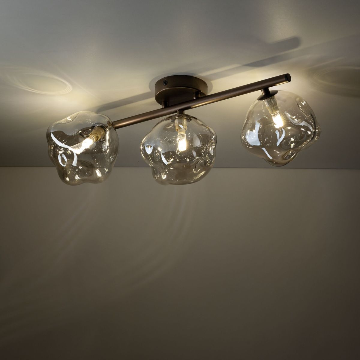 Brązowa lampa sufitowa Lava Brown z trzema kloszami G9. Klosze o organicznym kształcie wykonane z przezroczystego szkła, zamontowane na metalowej oprawie. Ujęcie z dołu, pokazujące szczegóły kloszy i ich rozmieszczenie.