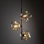 Brązowa lampa wisząca Lava Brown z trzema kloszami w kształcie nieregularnych brył, wykonana z przezroczystego szkła. Lampa umieszczona na poziomej metalowej rurze, zawieszona na czarnym przewodzie, w subtelnym oświetleniu.