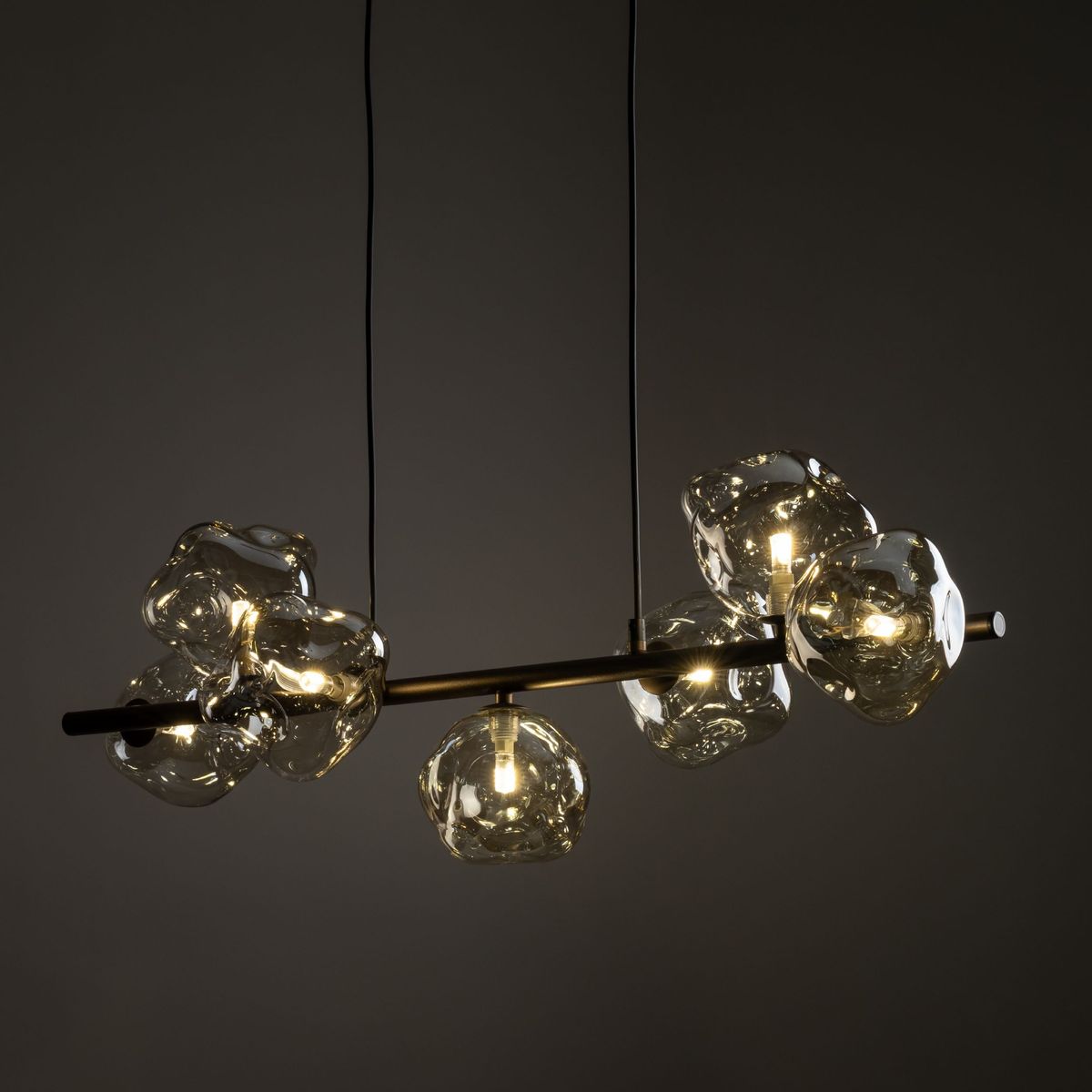 Brązowa lampa wisząca Lava Brown z siedmioma szklanymi kloszami w kształcie nieregularnych brył. Utrzymana na czarnym stelażu, zawieszona na dwóch cienkich linkach. Efektowne oświetlenie, idealne do nowoczesnych wnętrz.
