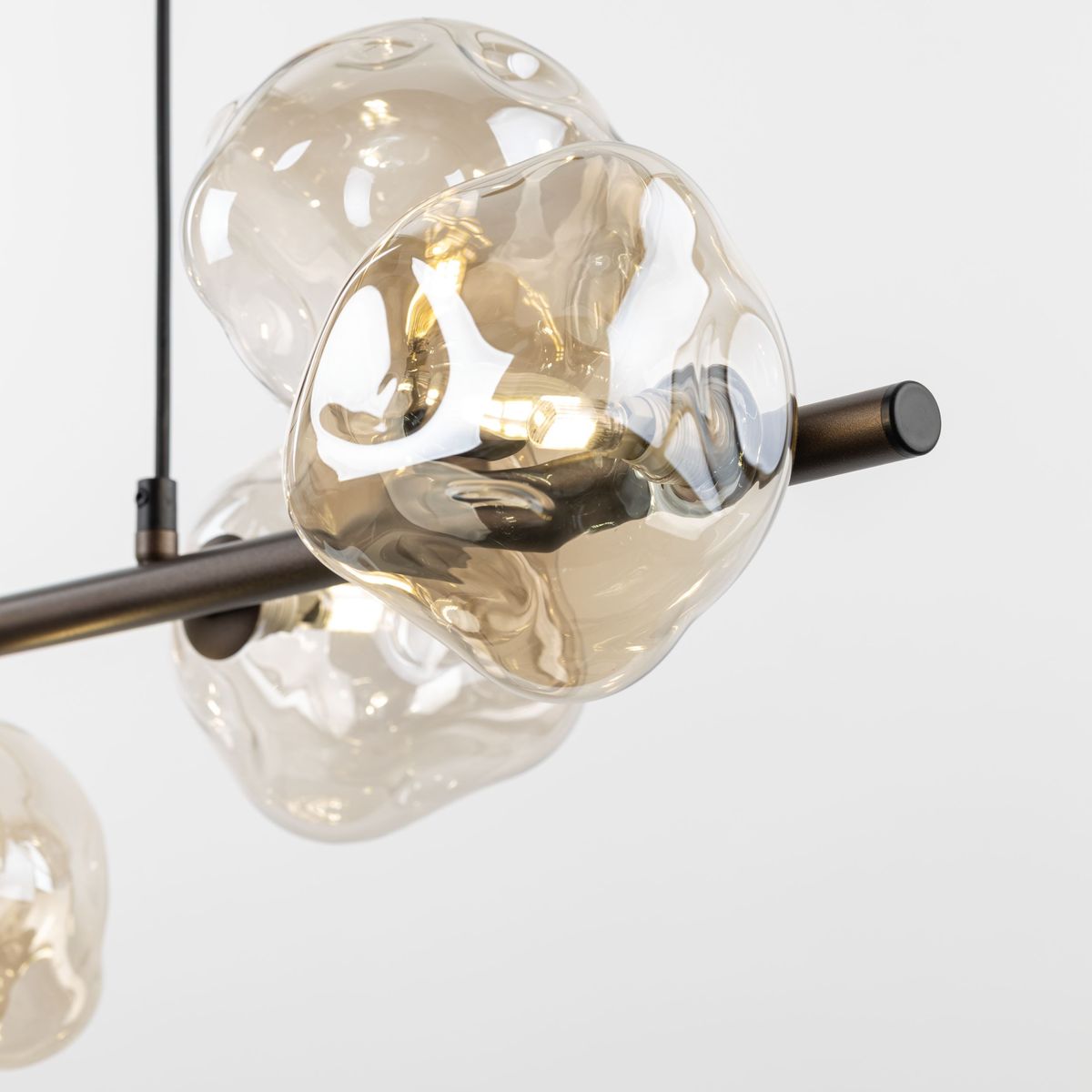 Lava Brown lampa wisząca z siedmioma kloszami w kształcie bąbelków, wykonany z przezroczystego szkła w odcieniu brązowym. Metalowy stelaż w kolorze brązowym. Klosze eksponują żarówki G9. Ujęcie z boku, ukazujące detale konstrukcji.