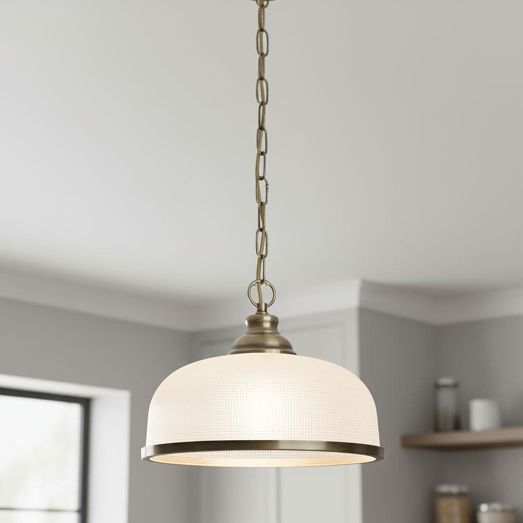 Lampa wisząca Bistro II w antycznym mosiądzu, z okrągłym kloszem w białym kolorze, zawieszona na łańcuchu. Klosz ma teksturowaną powierzchnię i metalowy brzeg, umieszczona w jasnym wnętrzu.