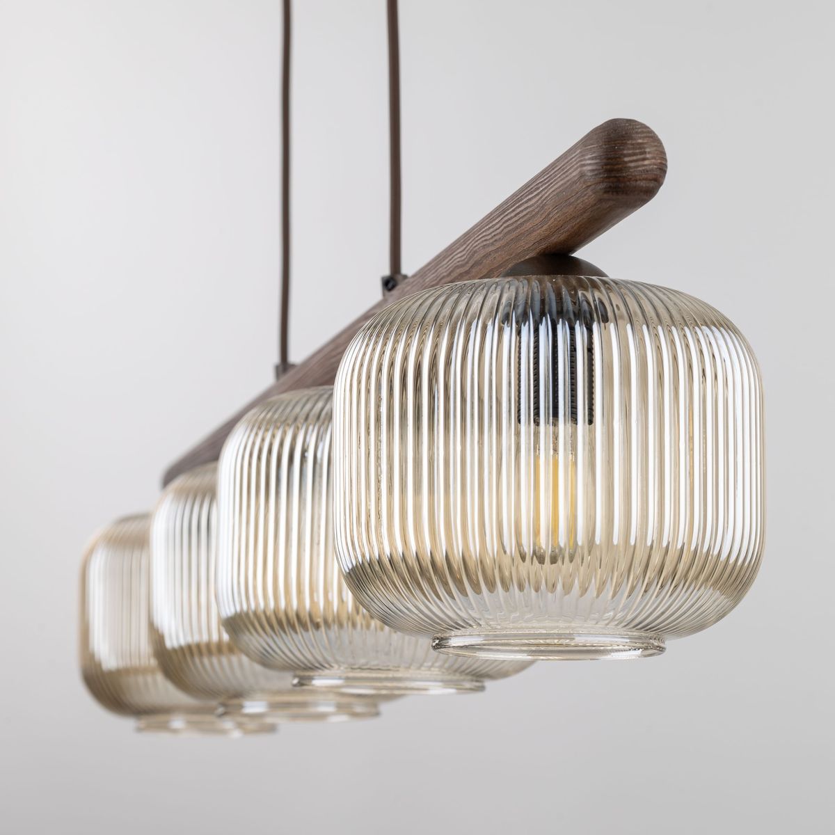 Lampa wisząca Salvia Brown TK11070 z czterema kloszami E14, w kolorze brązowym, z przezroczystego, żłobkowanego szkła. Posiada drewniany uchwyt oraz zawieszenie, w aranżacji na jednolitym tle.