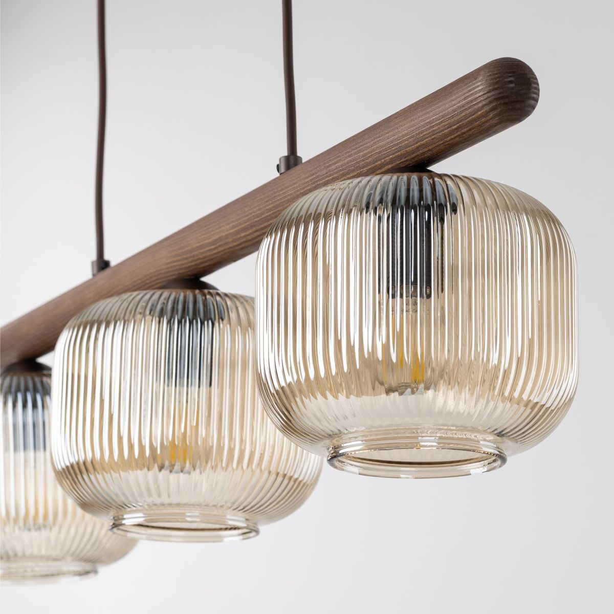 Lampa wisząca Salvia Brown z trzema kloszami E14, w kolorze brązowym. Klosze o zaokrąglonym kształcie, teksturowanej powierzchni, zawieszone na drewnianym stelażu. W tle jasne, neutralne tło.