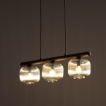 Lampa wisząca Salvia Brown z trzema kloszami na żarówki E14, umieszczona na brązowym uchwycie. Klosze mają przezroczystą, żłobioną fakturę, a lampa wisi na dwóch cienkich przewodach, na ciemnym tle.
