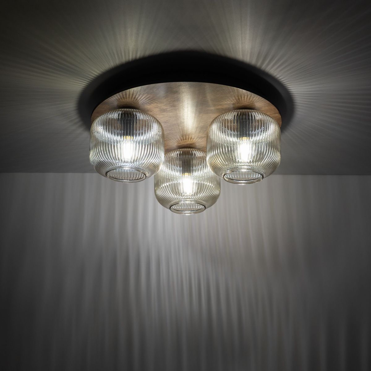 Brązowa lampa sufitowa Salvia Brown z trzema kloszami E14, wykonana z przezroczystego szkła z teksturowanym wykończeniem. Produkt zamontowany na okrągłej podstawie, emitujący rozproszone światło z efektownymi wzorami na suficie.