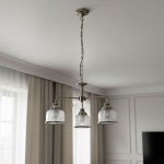 Lampa wisząca Bistro II w kolorze antycznego mosiądzu, z trzema szklanymi kloszami, zawieszona na łańcuchu. Klosze mają teksturowaną powierzchnię i metalowe obręcze. Produkt umieszczony w jasnym wnętrzu z zasłonami.