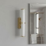 Kinkiet Clamp LED IP44 w kolorze złotym, o prostokątnym kształcie, z przezroczystym kloszem, zamontowany na ścianie obok lustra. Klosz z teksturowanego szkła, metalowe wykończenie, stylowa konstrukcja.