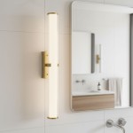 Kinkiet Clamp LED IP44 w kolorze złotym, o cylindrycznym kształcie, zamontowany na ścianie. Emisja światła przez przezroczystą osłonę. W tle widoczna łazienka z lustrem, umywalką i ręcznikiem.