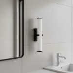 Kinkiet Clamp LED IP44 w kolorze czarnym, montowany na ścianie, z przezroczystym kloszem w formie cylindrycznej. Zainstalowany obok lustra na jasnej, gładkiej ścianie, idealny do łazienki.