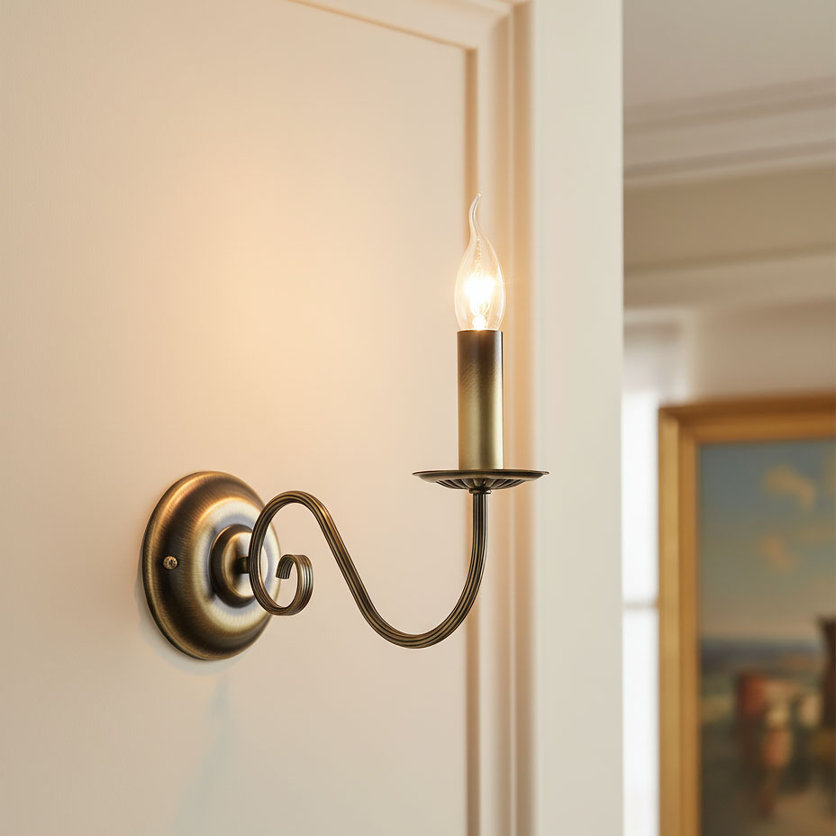 Kinkiet Asti 1-punktowy w kolorze patyny, montowany na ścianie. Posiada ozdobny kształt z falującym ramieniem i żarówkę w stylu świecy. Widoczna podstawa okrągła z detalami. Tło jasne, jednolite.