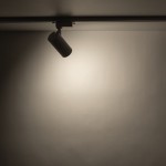 Reflektor spot Tracer 1xGU10 w kolorze białym, zamocowany na szynie 1-fazowej. W kształcie cylindrycznym, skierowany w dół, emitujący jasne światło na jednolitym tle.