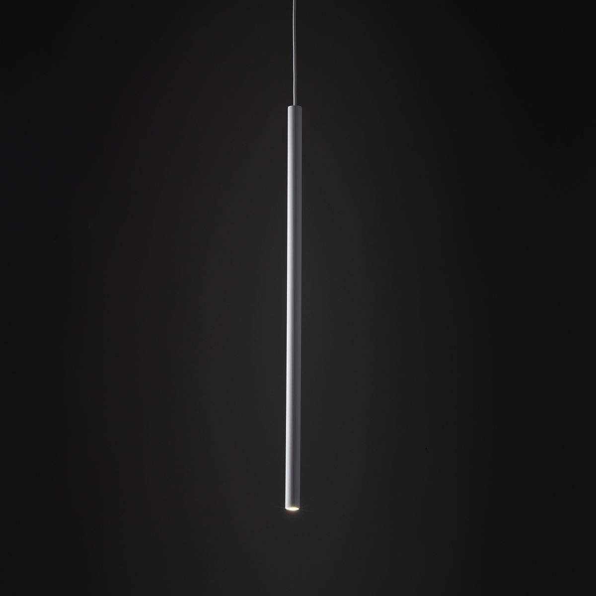 Lampa wisząca Tracer, 1-fazowa, biała, o cylindrycznym kształcie. Ujęcie z dołu, wisząca na cienkim przewodzie, emituje światło z dolnej krawędzi. Tło ciemne, co podkreśla minimalistyczny design lampy.