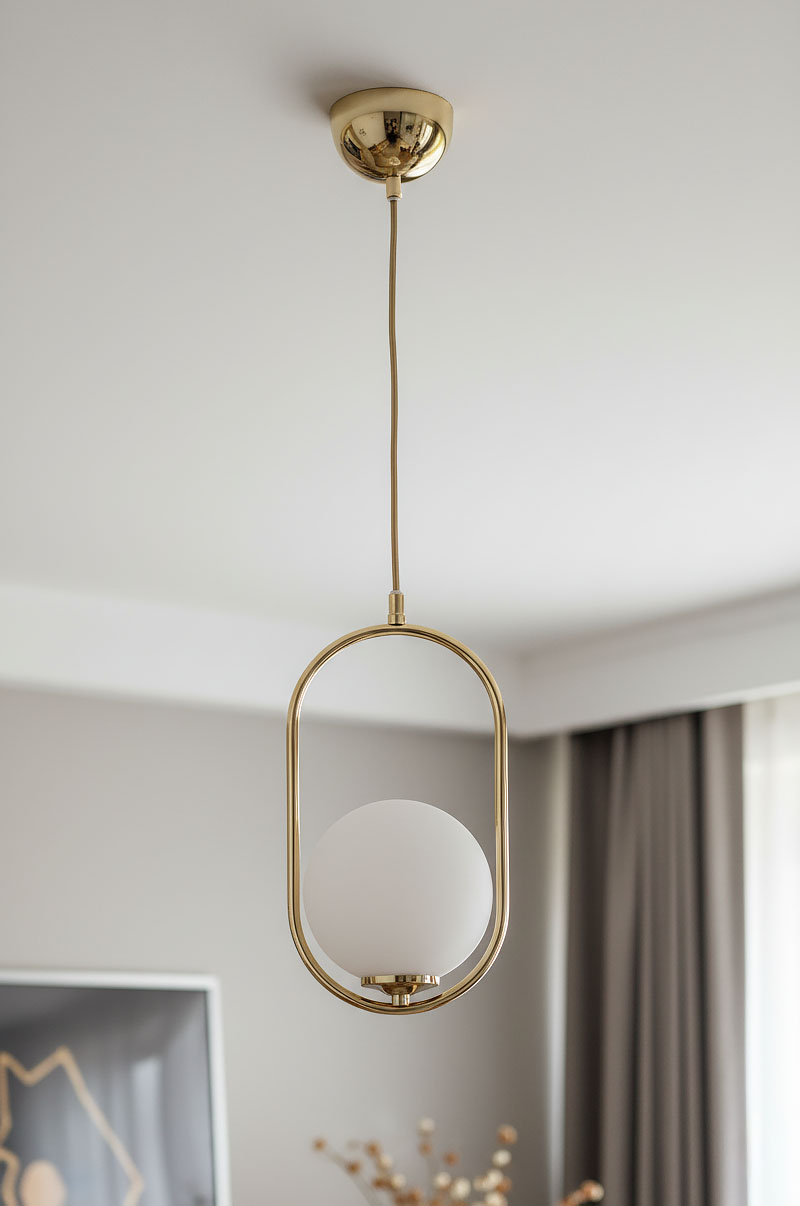 Lampa wisząca Noval M w kolorze złotym z białym, okrągłym kloszem. Zawieszona na cienkim kablu, ma owalną podstawę. Klosz z mlecznego szkła umieszczony w metalowej ramie, stylowy element do nowoczesnych wnętrz.