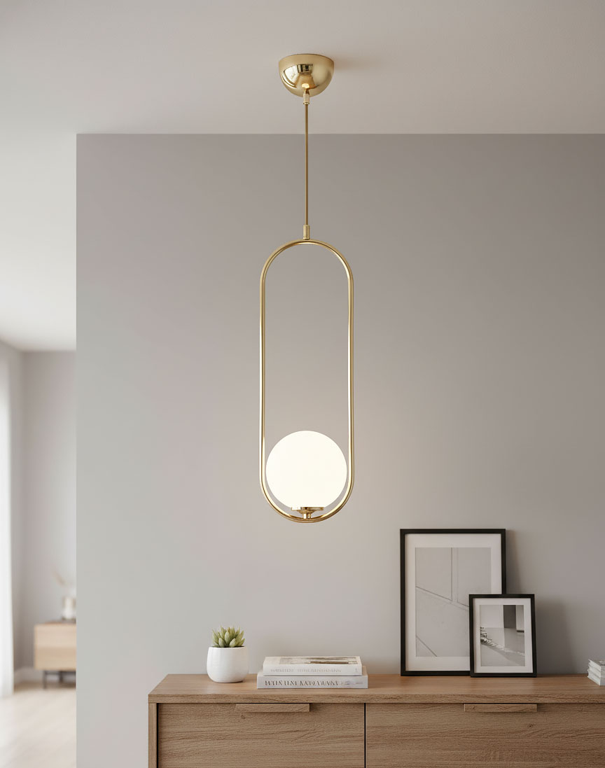 Lampa wisząca Noval L w złotym kolorze z okrągłym, białym kloszem. Zawieszona na cienkim drucie, w otwartej ramie. Tło w odcieniach szarości, meble drewniane z książkami i dekoracją roślinną.