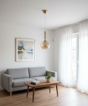 Lampa wisząca Grall D20 w kolorze złotym, z przezroczystym kloszem, zawieszona na cienkim przewodzie. Umieszczona w jasnym wnętrzu obok szarej kanapy i drewnianego stolika, w otoczeniu białych firan i obrazu w złotej ramie.