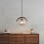 Lampa wisząca Korda 1-punktowa w kolorze złotym z przezroczystym kloszem, zawieszona na czarnym przewodzie. Ujęcie frontalne, z widoczną dekoracyjną oprawą oraz delikatnym światłem. Produkt umieszczony nad drewnianym meblem w minimalistycznym wnętrzu.