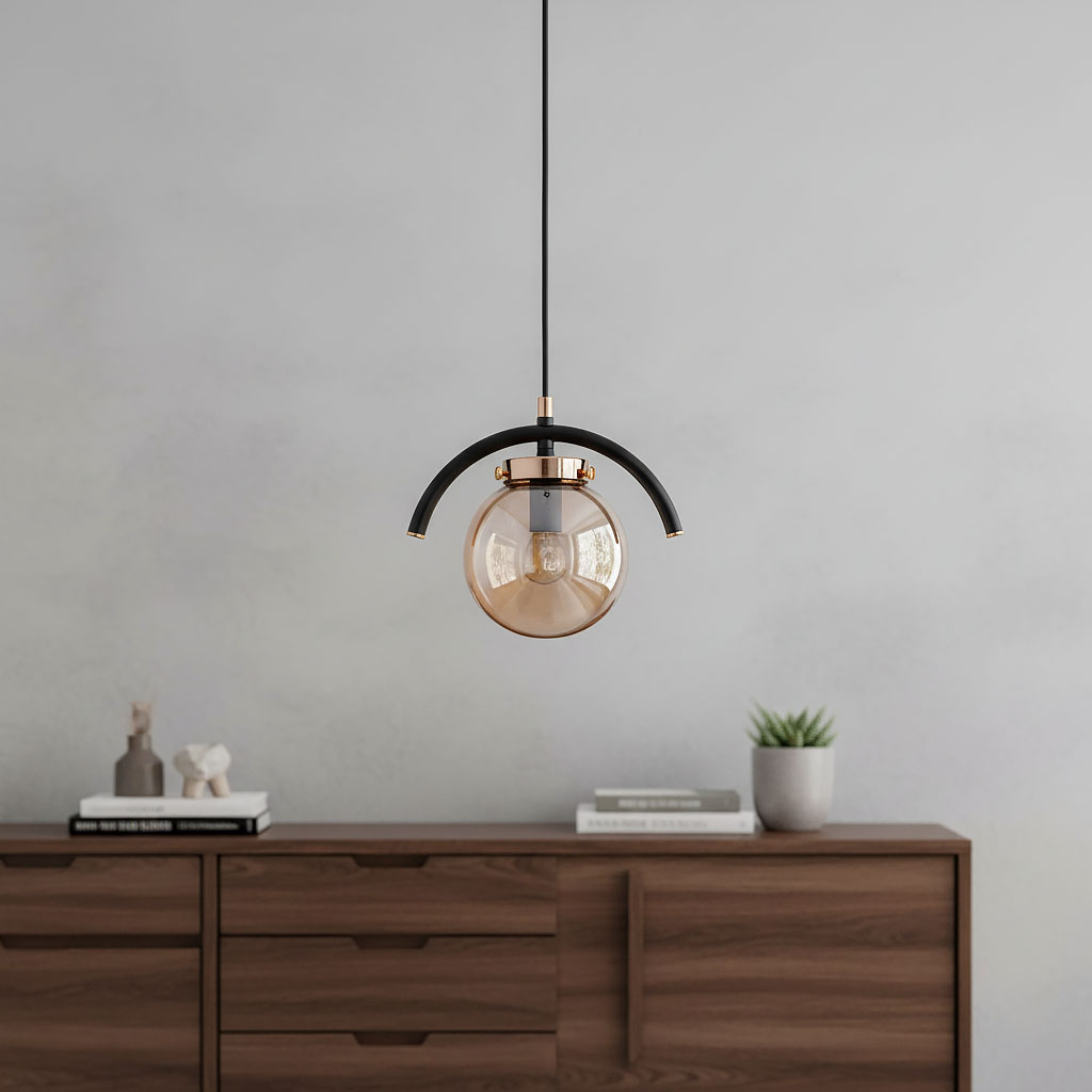 Złota lampa wisząca Korda 1-punktowa z przezroczystą kulistą kloszem, zawieszona na czarnym przewodzie. Kształt owalny z metalowym wykończeniem. Tło w odcieniach szarości, drewniana komoda z dekoracjami w dolnej części.