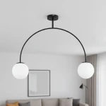 Czarna lampa wisząca Bendo z dwoma kulistymi kloszami w białym kolorze. Ułożona w łuk, zawieszona na czarnym stelażu. Widoczna w nowoczesnym wnętrzu, na tle jasnej ściany i szarej kanapy.