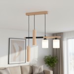 Lampa wisząca Nimir z naturalnego drewna, z dwoma oprawami E27 i dwoma GU10. Elementy w kształcie cylindrów, z matowymi kloszami. Ujęcie z góry, lampa zawieszona na czarnych kablach, w nowoczesnym wnętrzu z rośliną w tle.